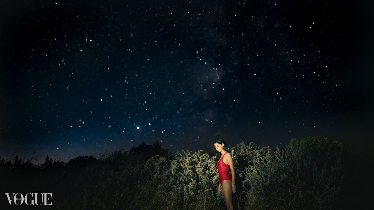 A distant figure in red stands illuminated beneath a star-filled night sky.